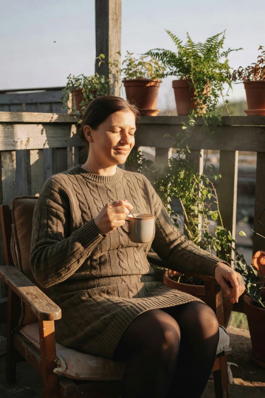 Woman wearing an olive cable-knit sweater dress with black tights, seated and holding a mug, showcasing a cozy office-ready layered look