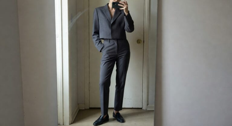 22 Trendy Work Outfit Ideas For Women Who Want A More Fashion Forward Office Look Woman taking mirror selfie in cropped gray blazer over bare skin, high-waisted beige trousers with hands in pockets, and black loafers on wooden floor inside doorway