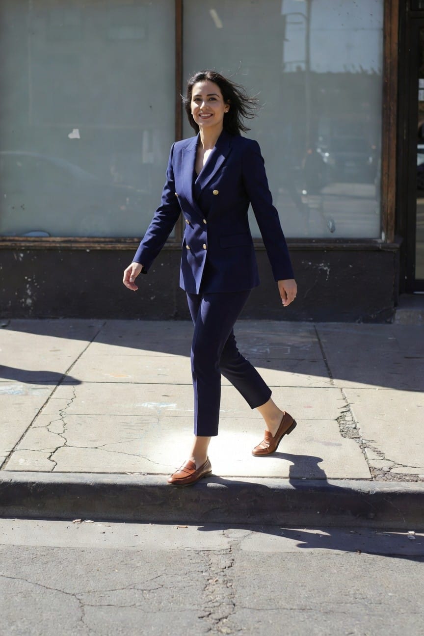 Woman in navy blue double-breasted blazer suit with slim ankle pants and brown leather loafers, walking confidently