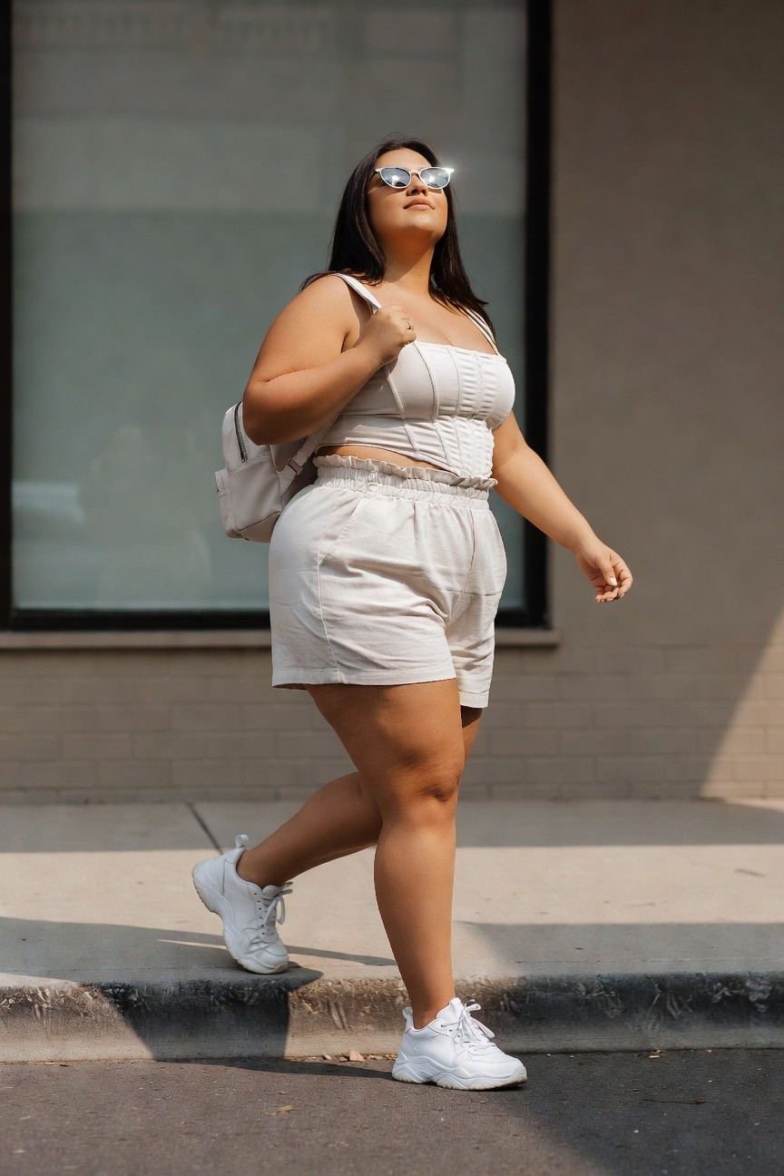 Woman in white outfit and sneakers walking on sunny city sidewalk.