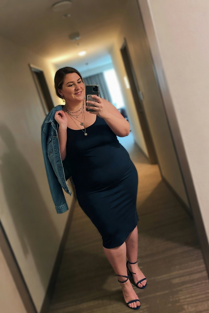 Woman in navy dress holding denim jacket and phone in hallway.