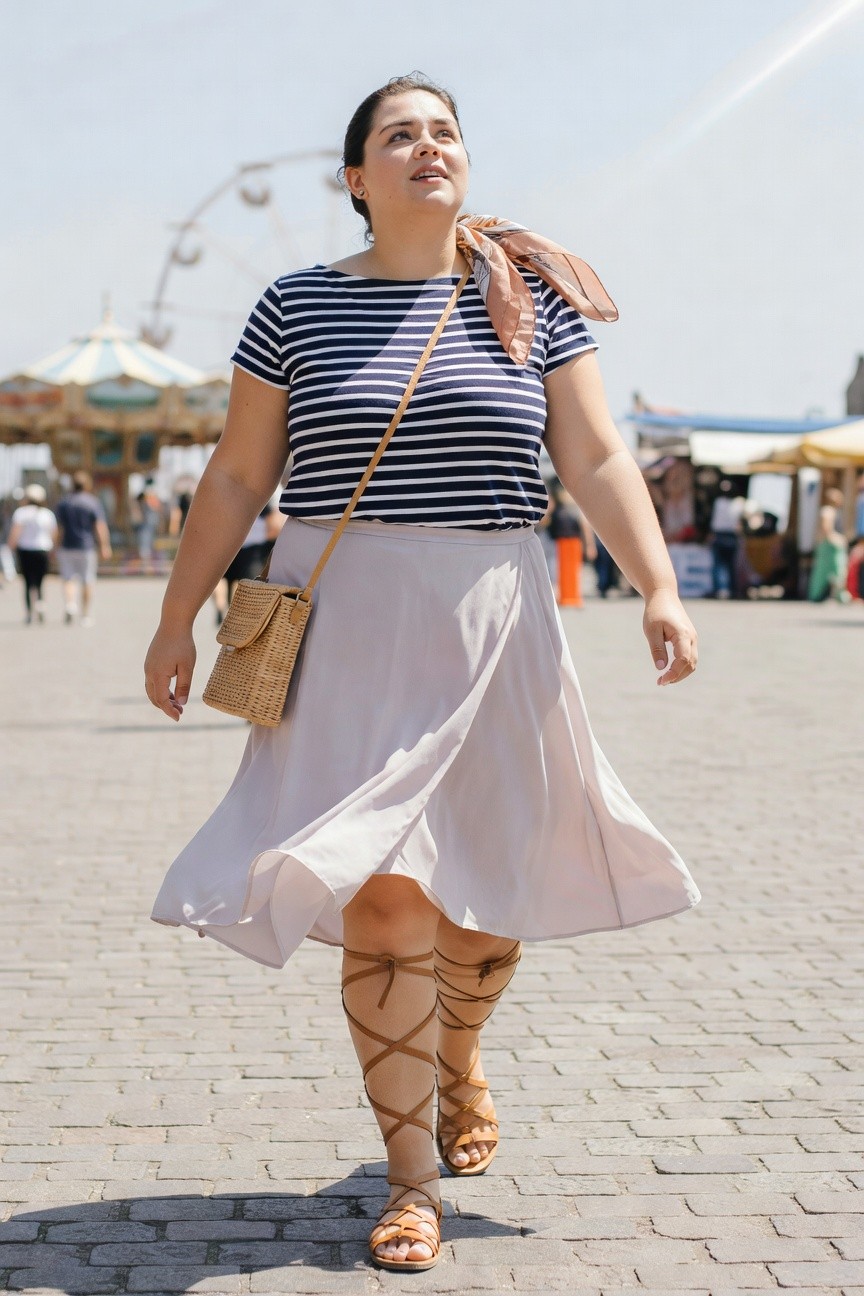 Woman in striped top and flowing white skirt walks at fair.