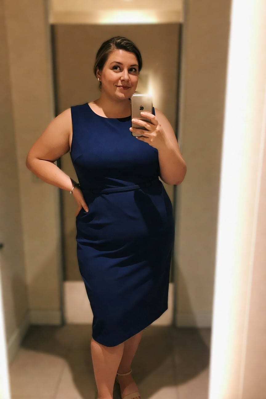 Woman in blue dress taking a mirror selfie with a smartphone.