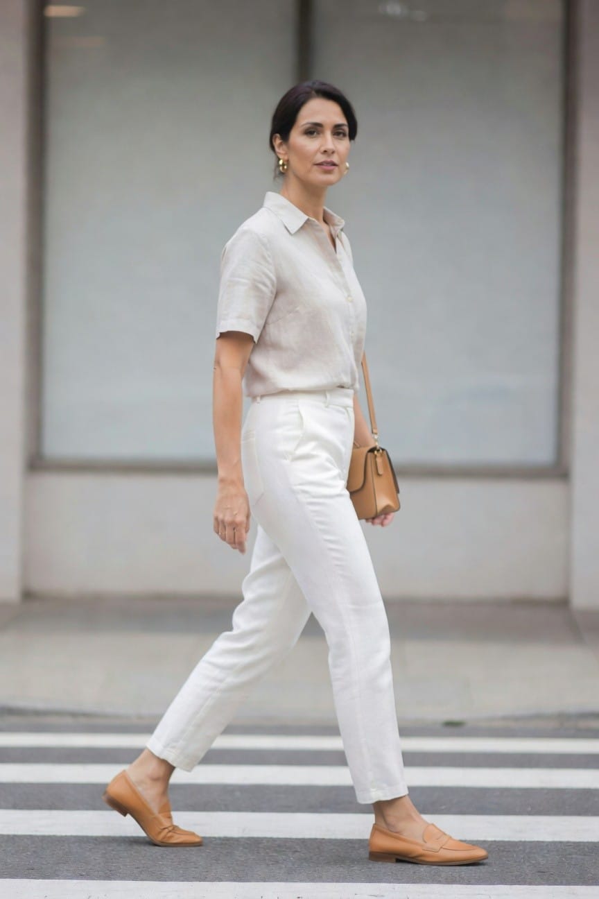 Woman in white linen outfit and tan loafers crossing street.