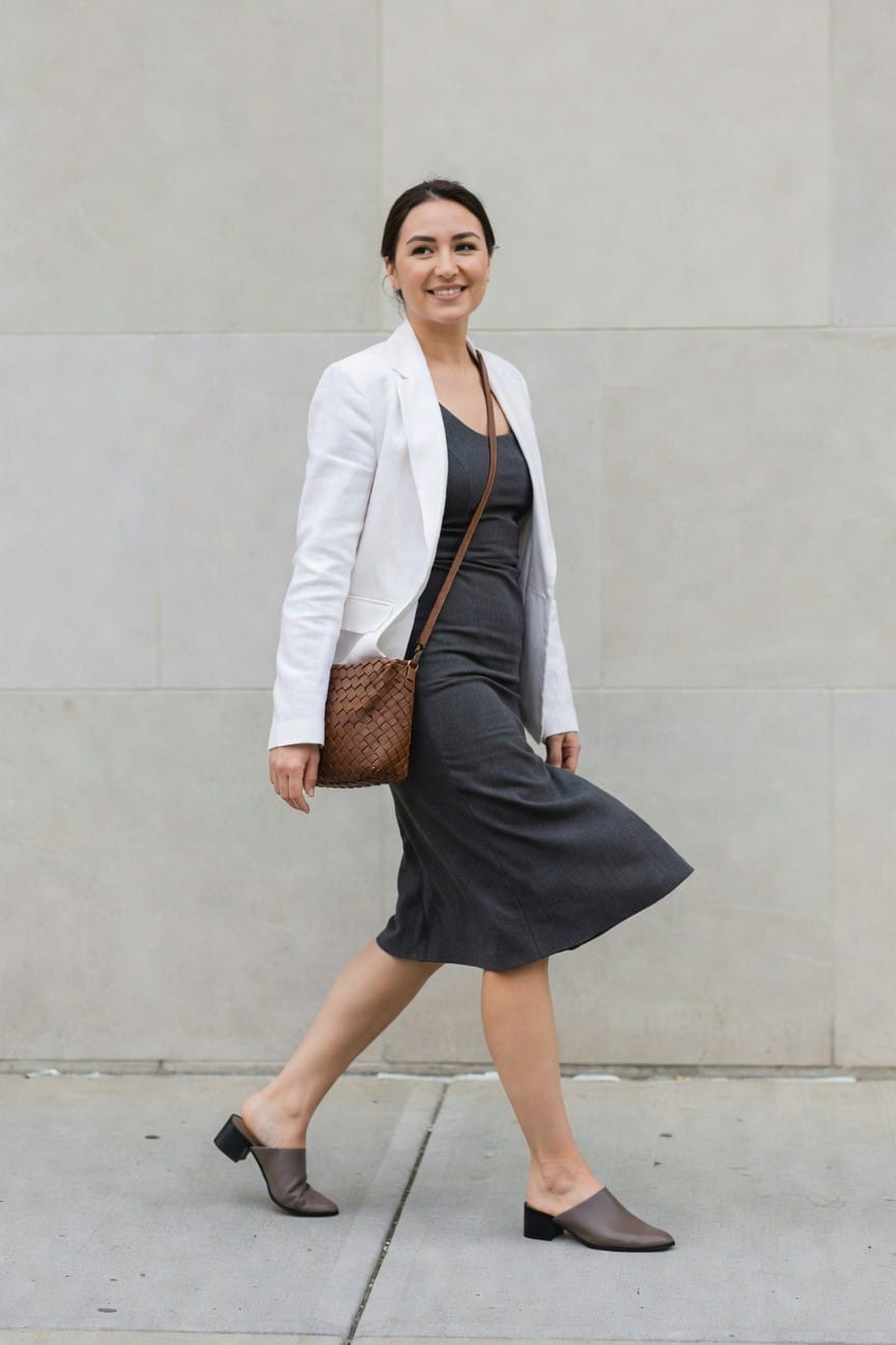 Woman in white blazer and gray dress with brown woven bag.