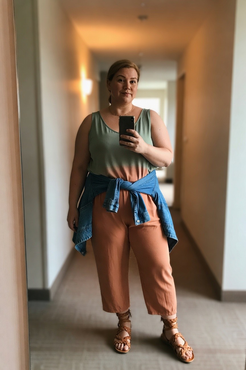 Woman in green-orange tank top and rust pants taking mirror selfie.