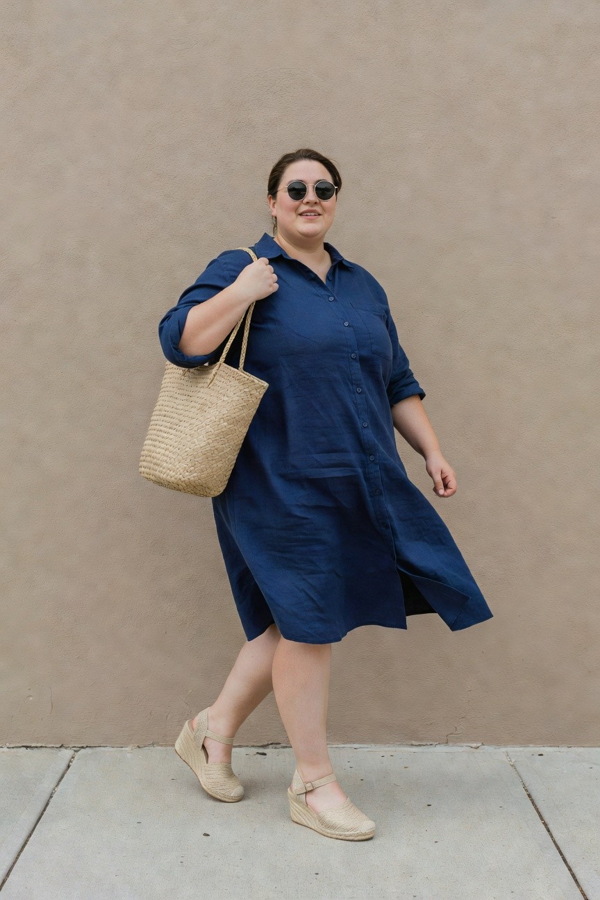 Woman in navy blue shirt dress holding woven tote bag outdoors.