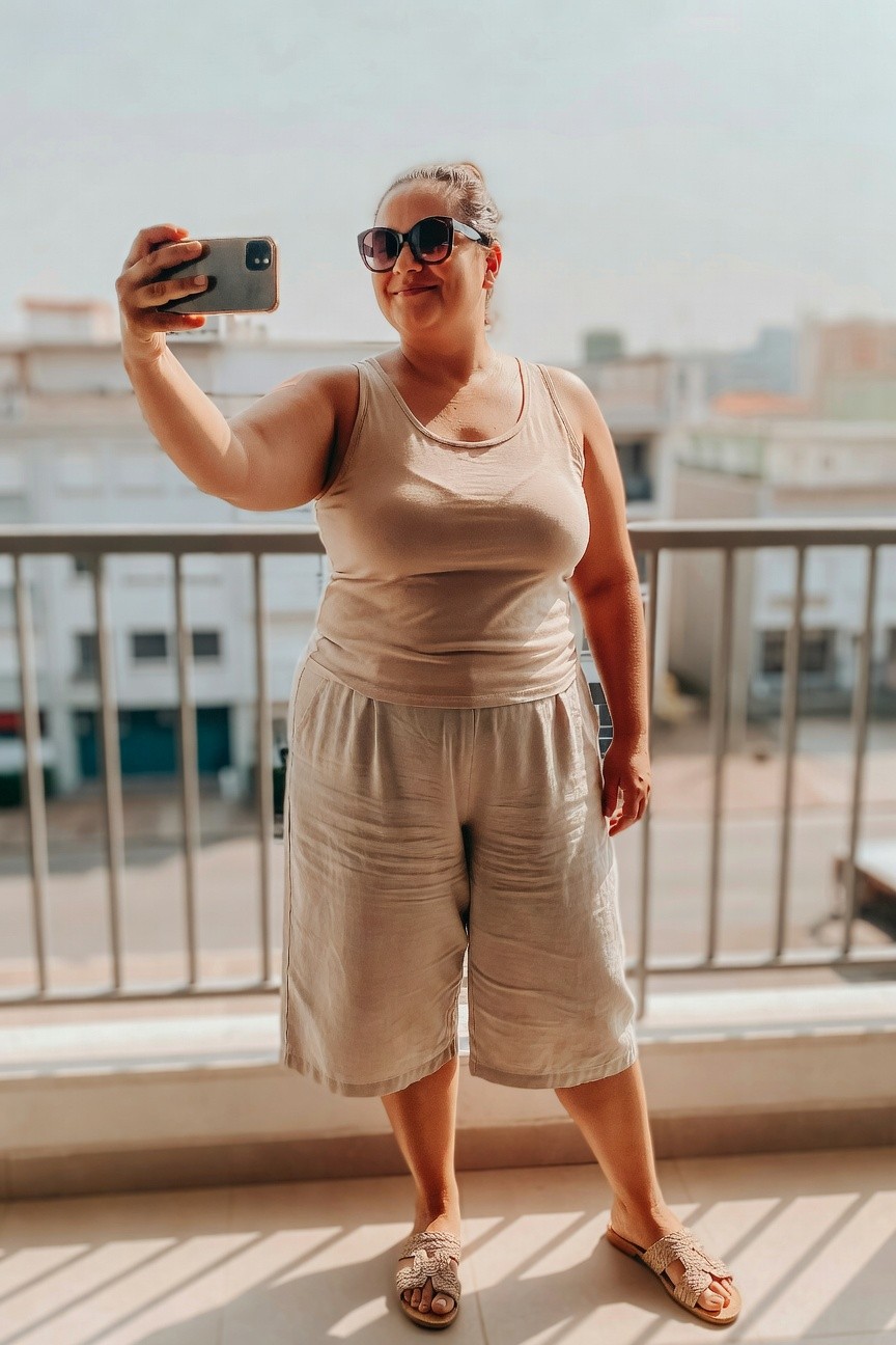 Woman in beige outfit taking a selfie on a sunny balcony.