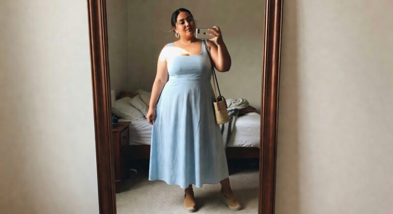 Woman wearing a pale blue midi sundress with thin straps and a flowing A-line skirt paired with beige espadrille wedges and a woven crossbody bag