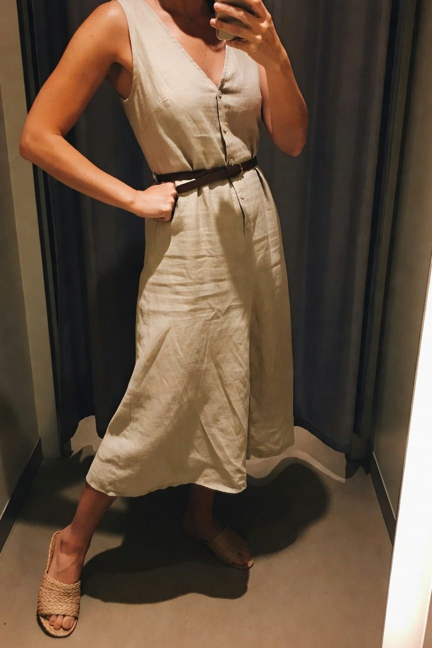 Woman in beige linen dress with brown belt taking a mirror selfie.