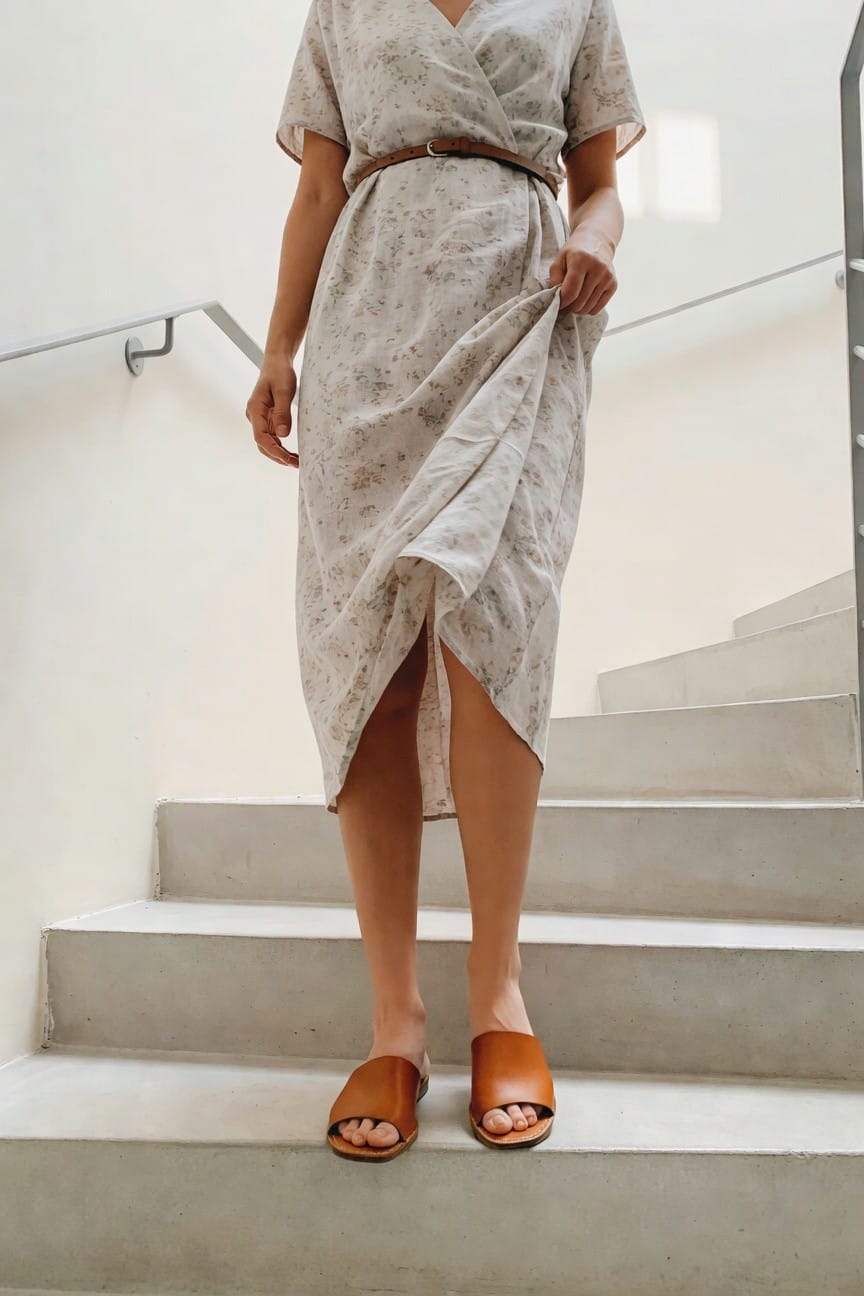 Woman in floral wrap dress and brown sandals on concrete stairs.