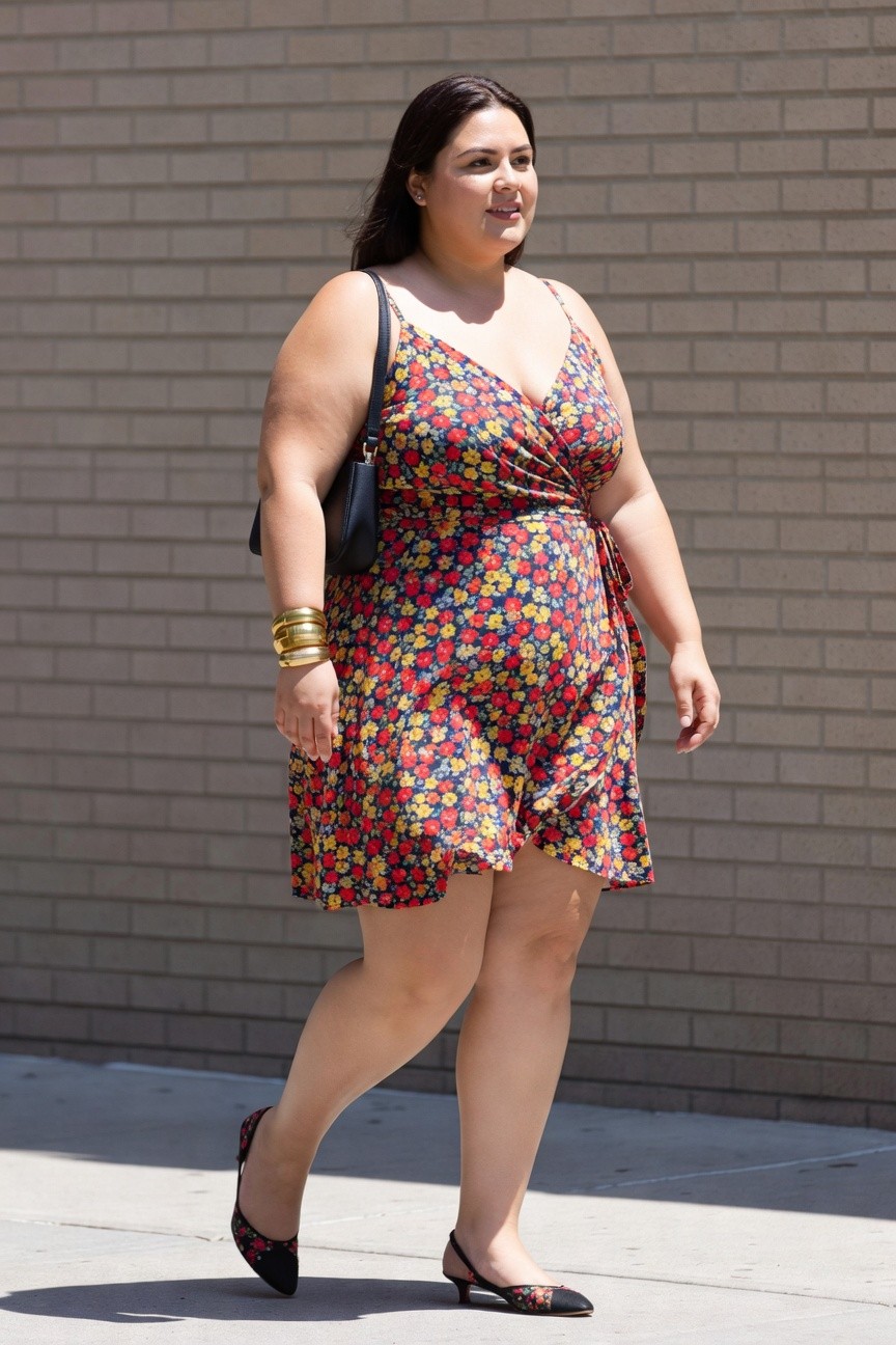 A plus-size woman in a floral wrap dress and heels walks outdoors.