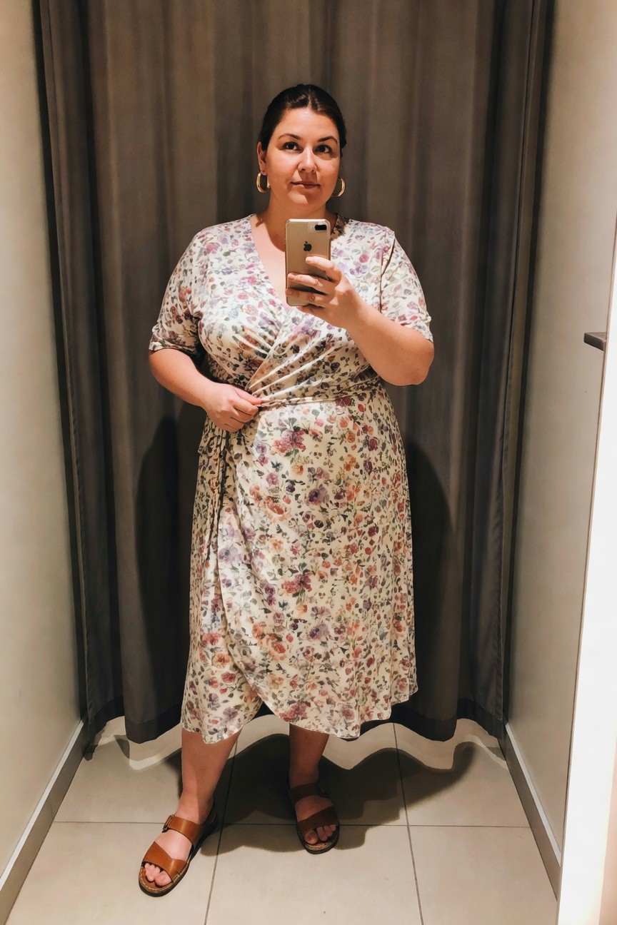 Woman in floral wrap dress taking mirror selfie with smartphone.