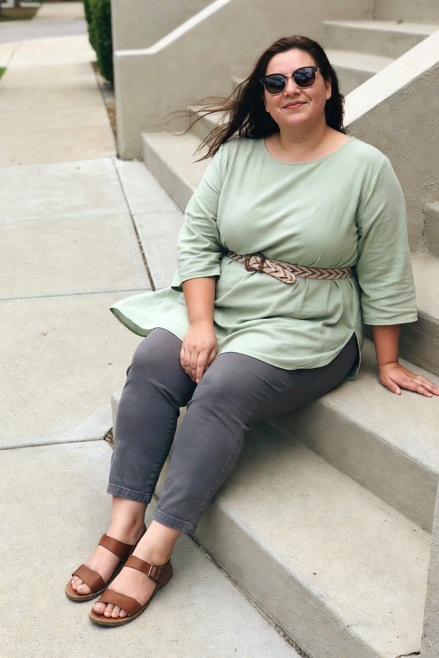 Woman in light green top and gray pants seated on concrete steps.