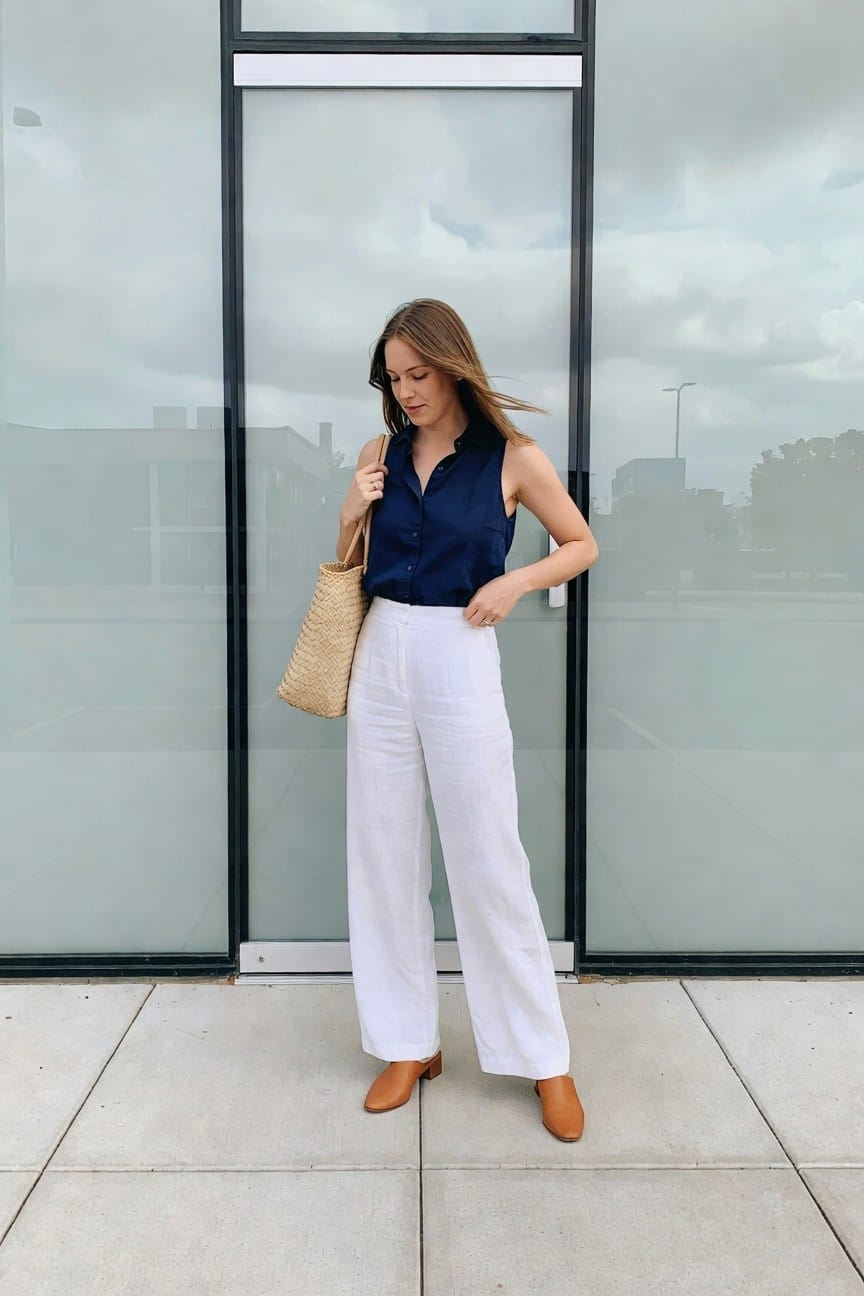 Woman in navy sleeveless top and white wide-leg pants with woven bag.