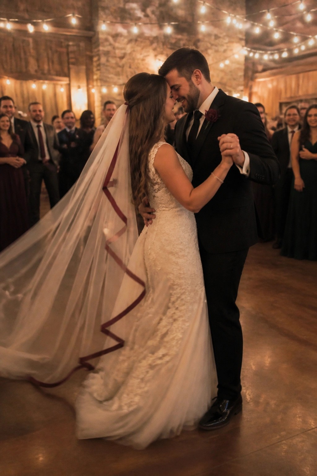 Bride in lace gown with veil dances closely with groom in black suit.