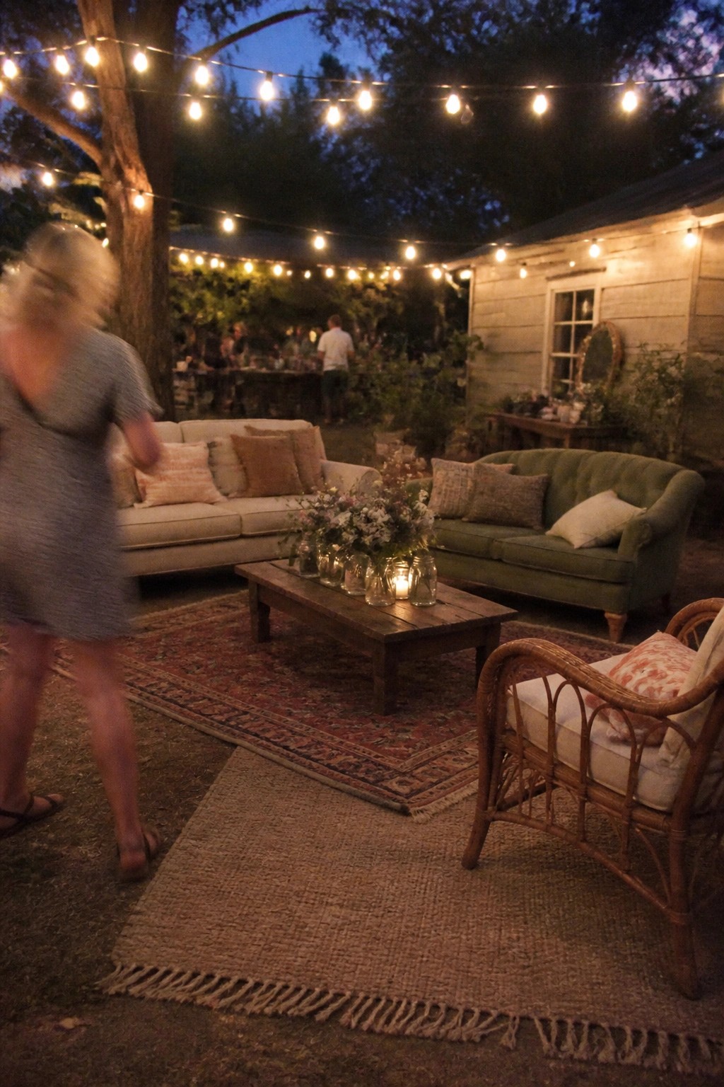 Outdoor wedding reception lounge with string lights sofas rugs and mason jar flowers at dusk