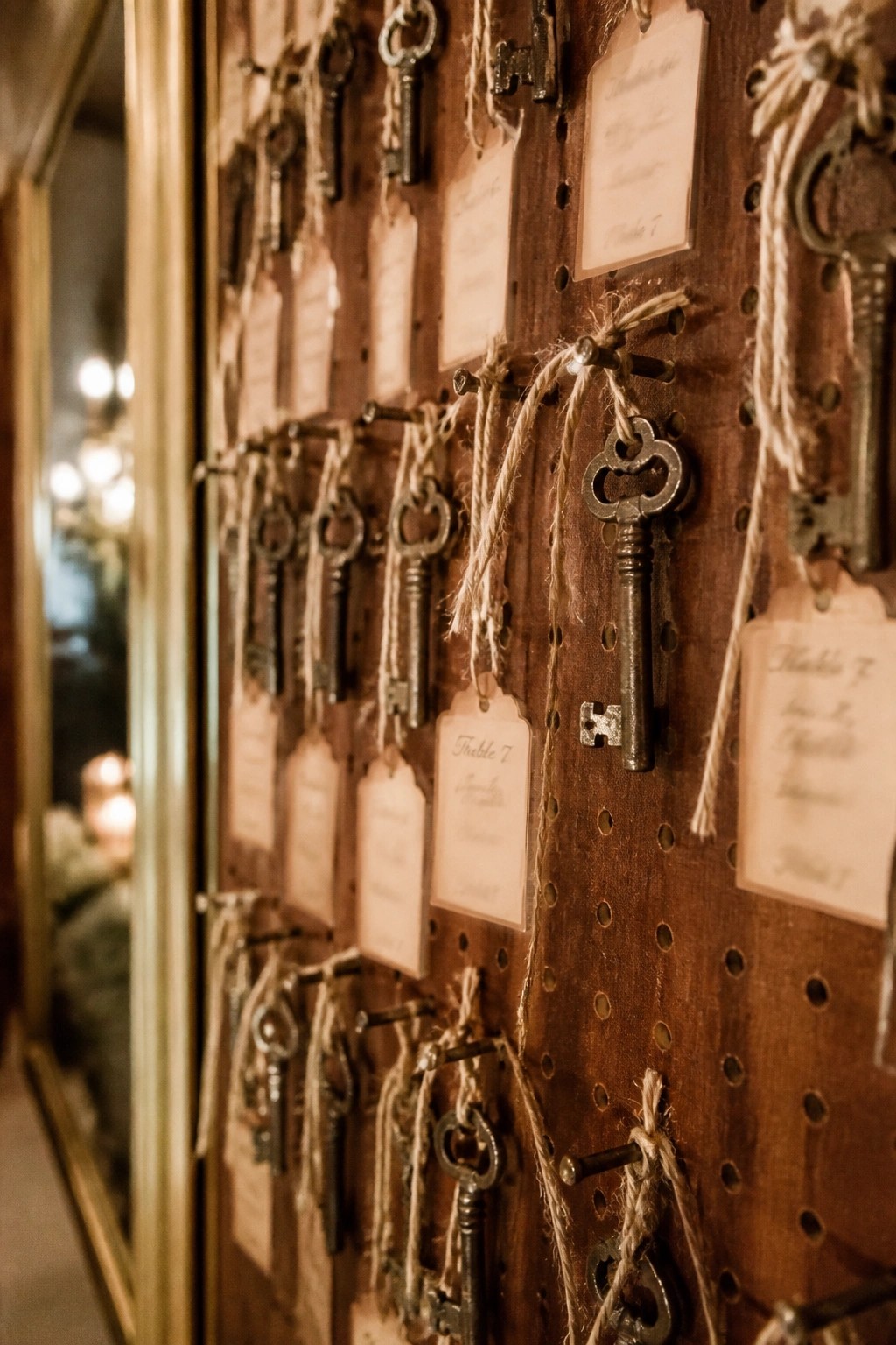 Close up of a rustic wooden board displaying vintage skeleton keys on twine with table number tags for wedding seating.