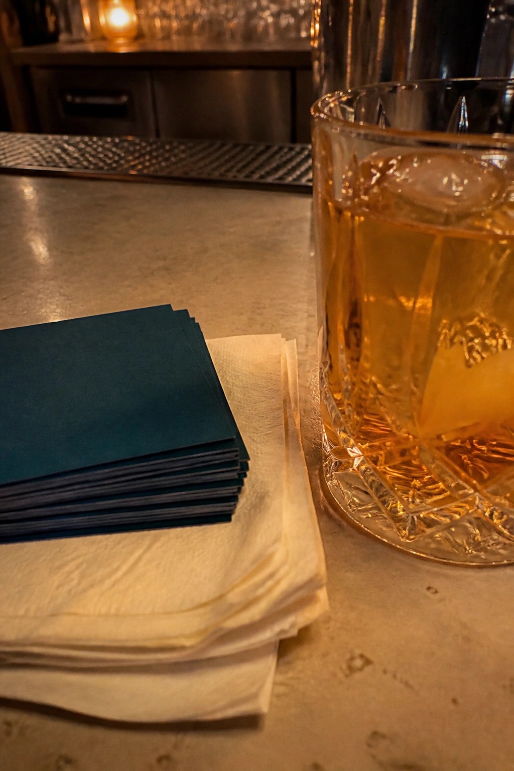 Close up of dark teal napkins stacked on white ones beside a glass of whiskey on a stone bar at a modern wedding reception