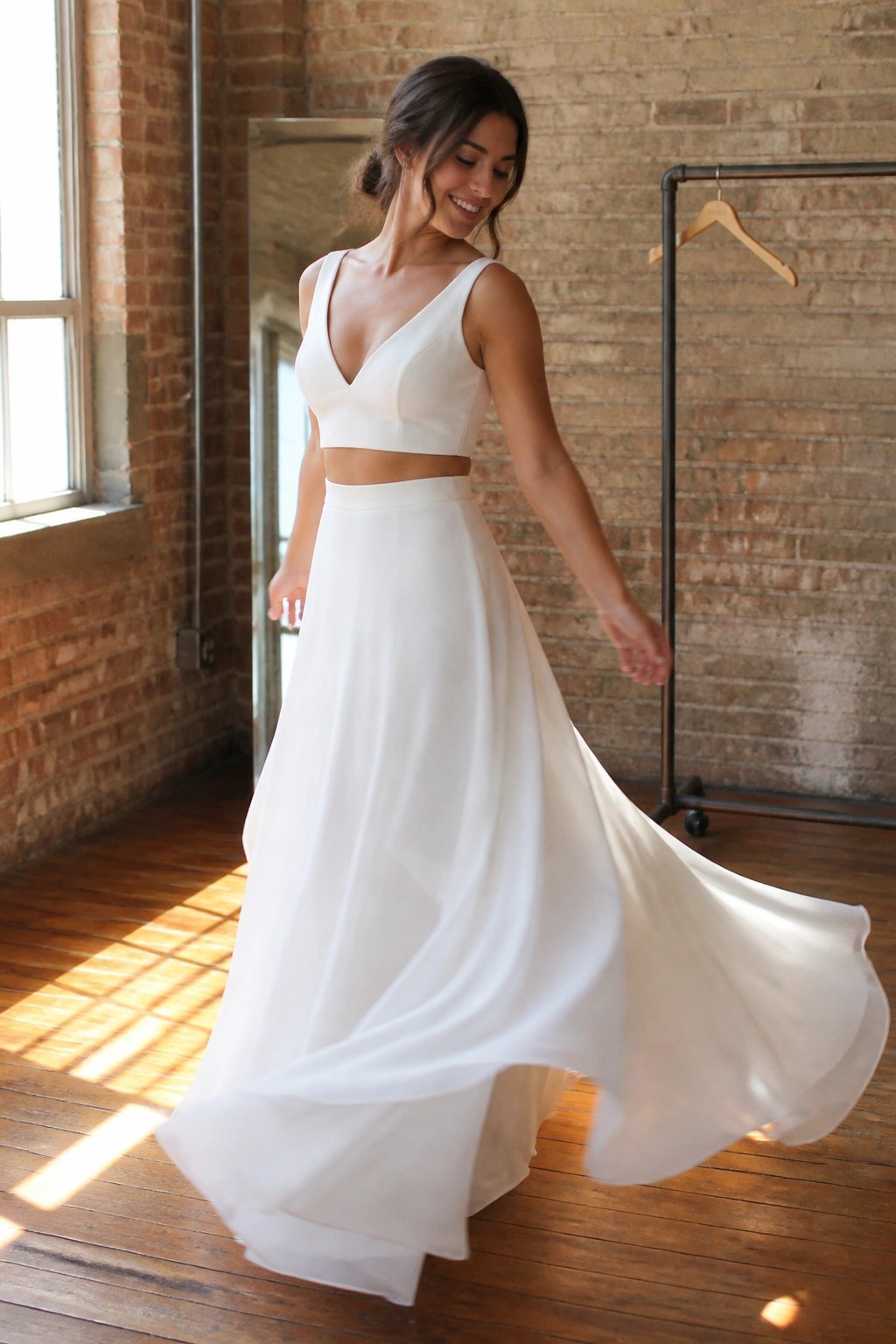 Bride in flowing white two piece wedding dress twirling in sunlit brick studio with wooden floors