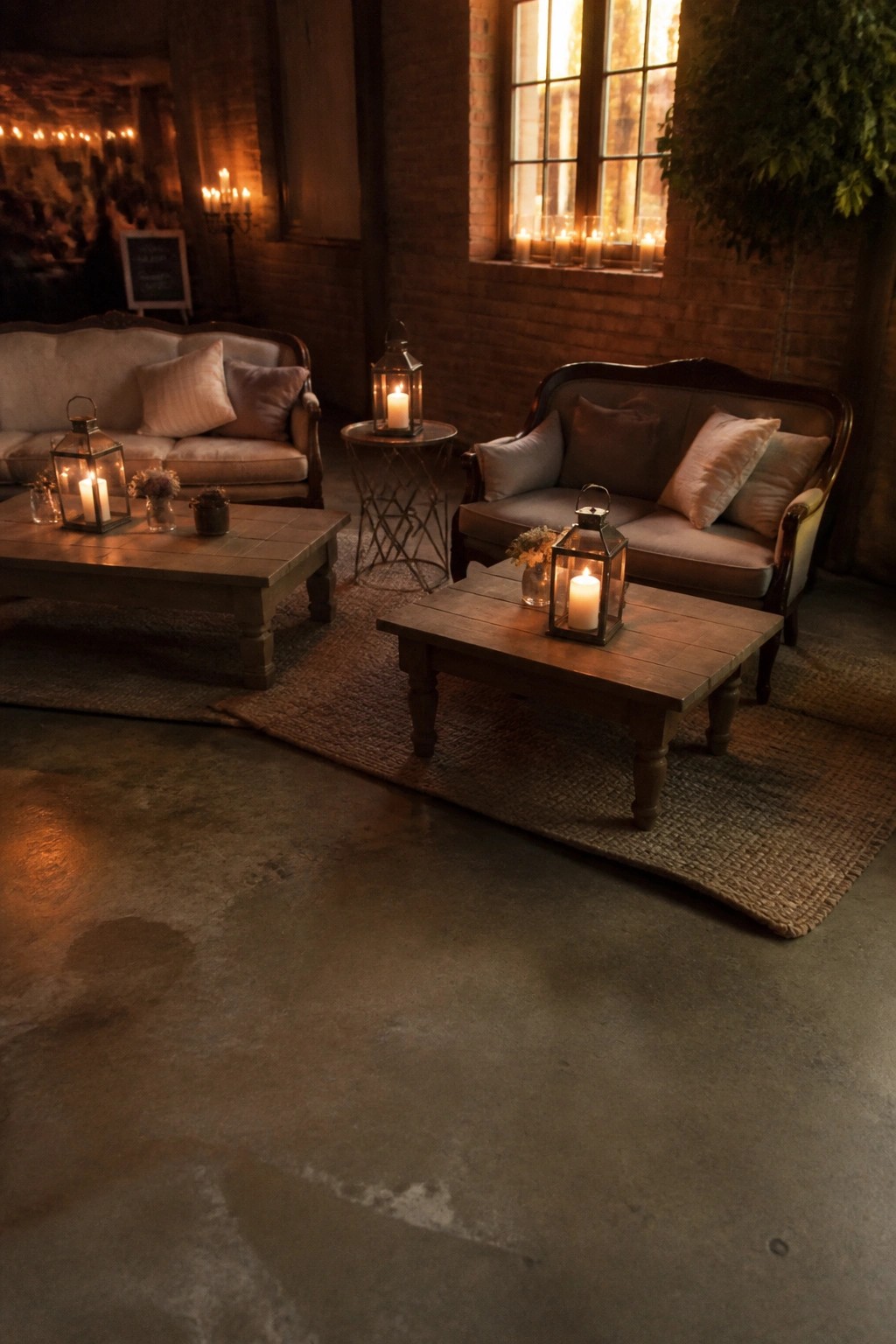 Cozy vintage lounge with two sofas, wooden coffee tables, and glowing lanterns set against brick walls in a warmly lit wedding reception space