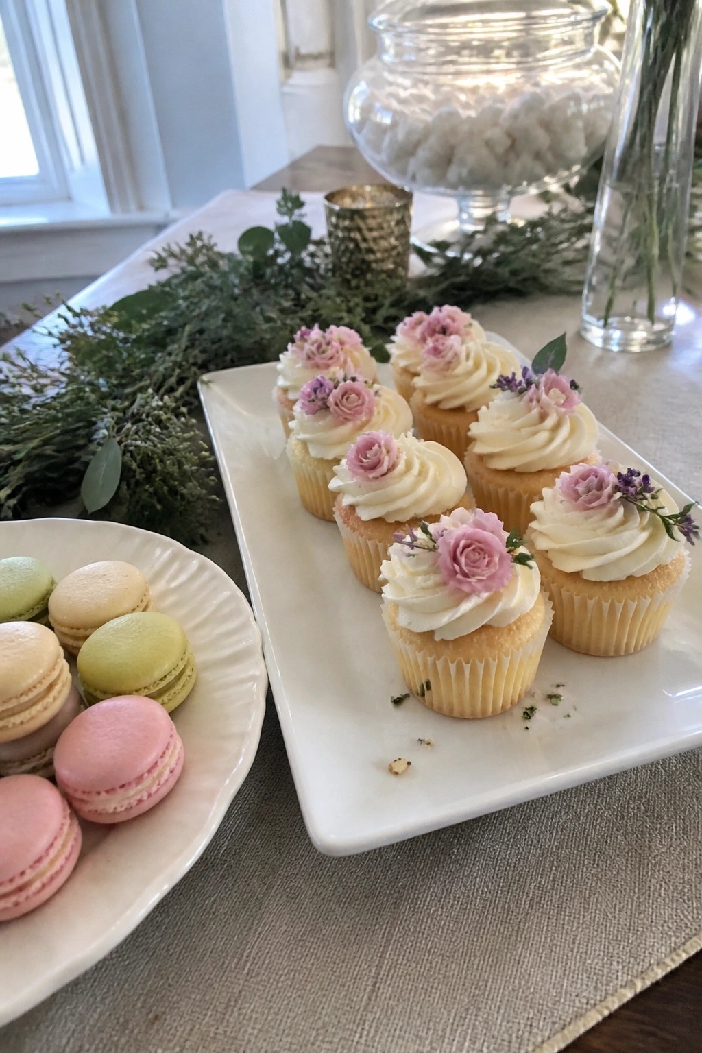 Pastel macarons and floral topped cupcakes arranged on a table with greenery for a garden wedding dessert display