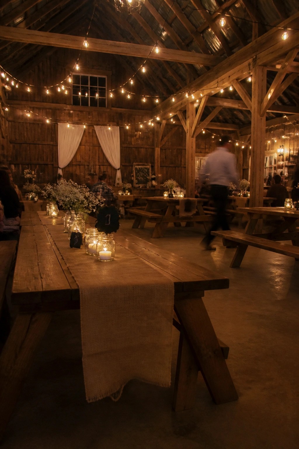 Rustic barn wedding venue with string lights wooden tables burlap runners and mason jar centerpieces at night