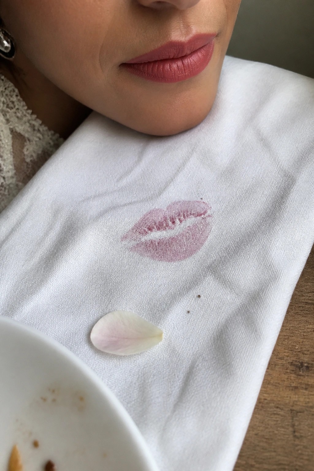 Close up of a bride with soft pink matte lips and a matching lipstick kiss print on a white napkin beside a flower petal