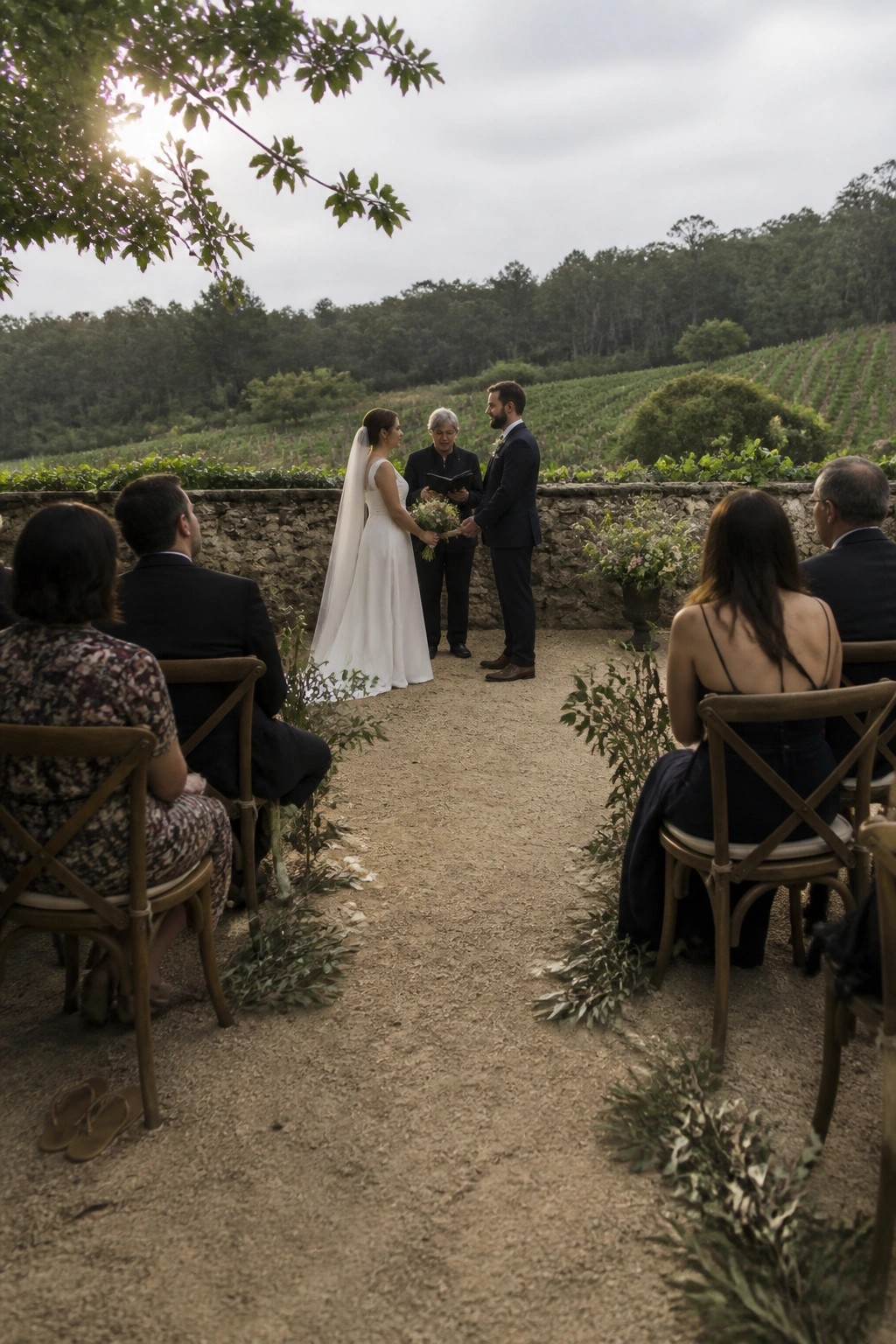 Bride and groom exchange vows outdoors in a vineyard with a small group of seated guests and rolling hills in the background