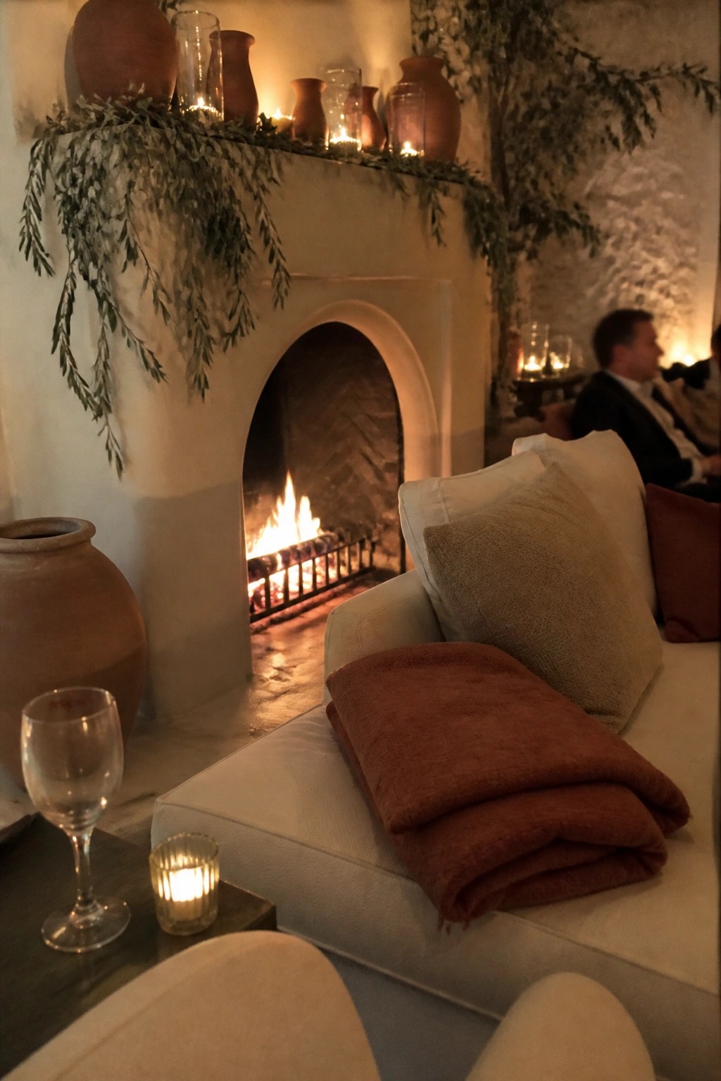 Cozy wedding lounge with white fireplace terracotta pots olive greenery rust blanket and cream sofa in warm candlelight