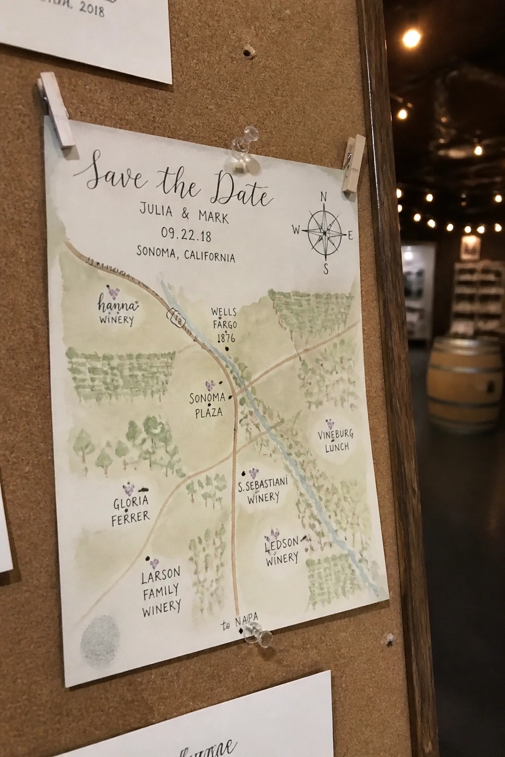 Watercolor map save the date card for Julia and Mark pinned to a corkboard with Sonoma wineries marked in green tones