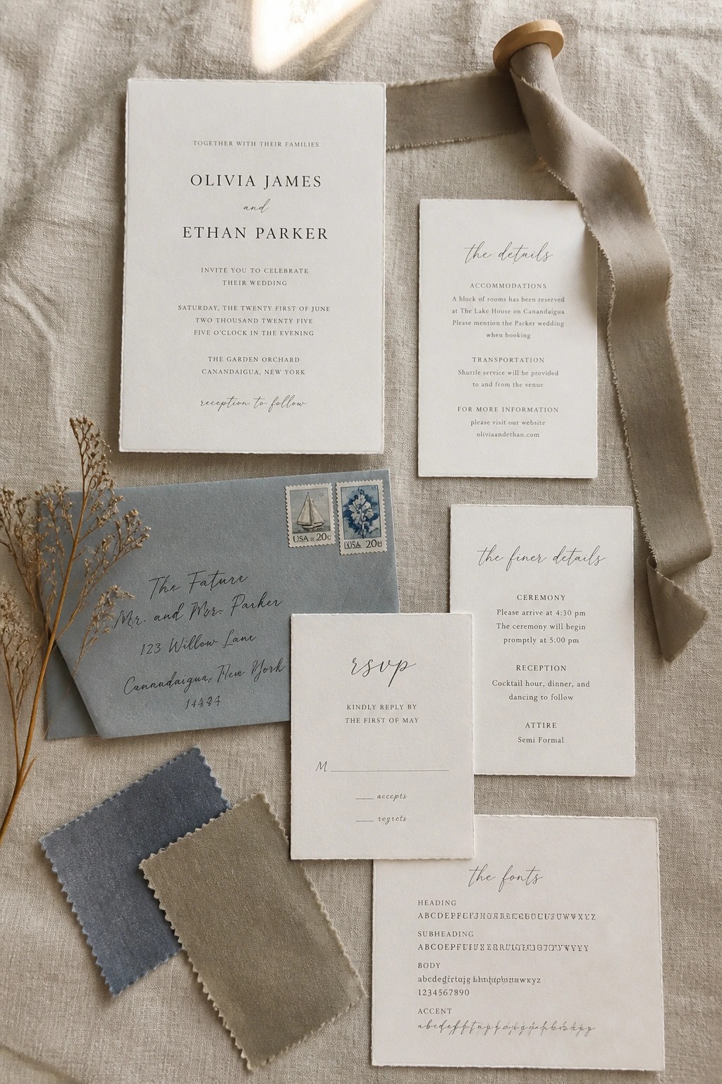 Flat lay of elegant wedding invitations in soft white and dusty blue with fabric swatches, dried flowers, and a silk ribbon on linen.
