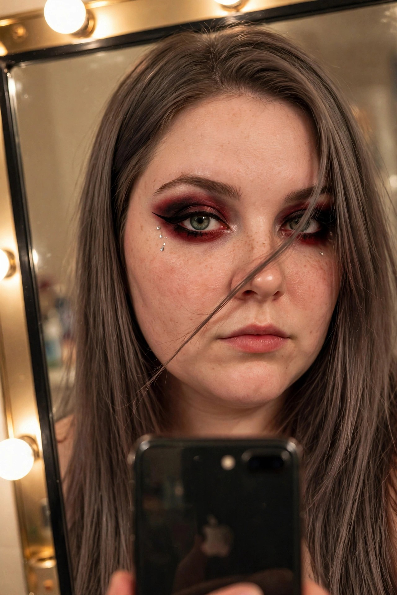 Close up of dramatic red and black smoky eye makeup with winged liner and three small rhinestones placed under the left eye.
