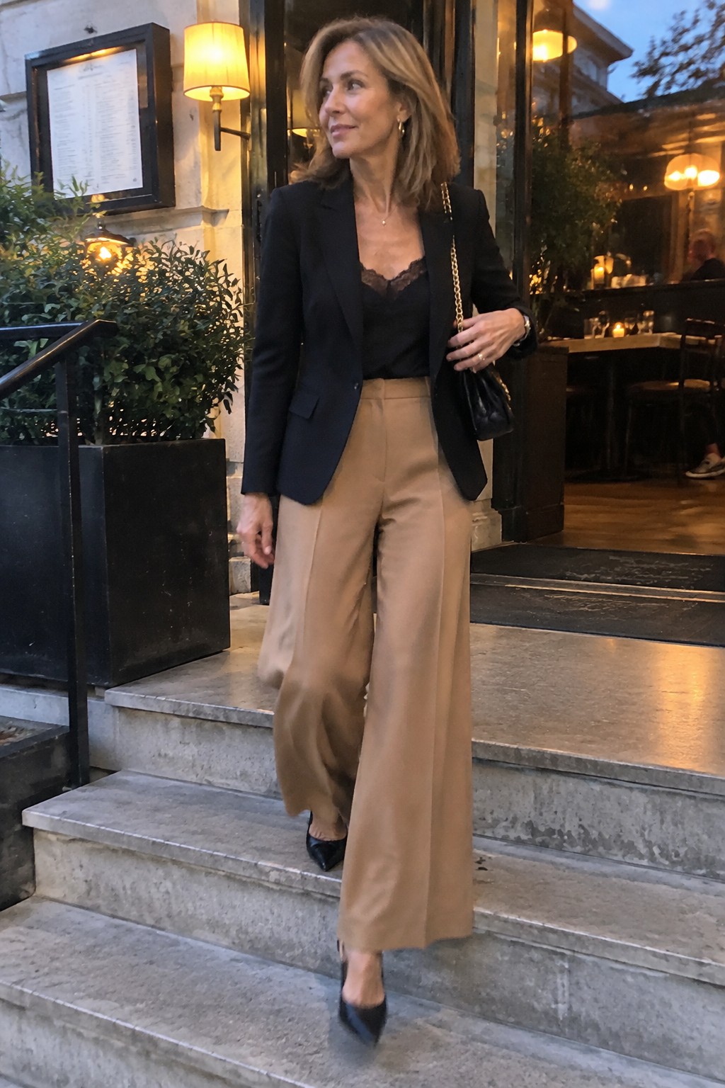 Woman in black blazer and tan wide-leg trousers on stone steps at dusk