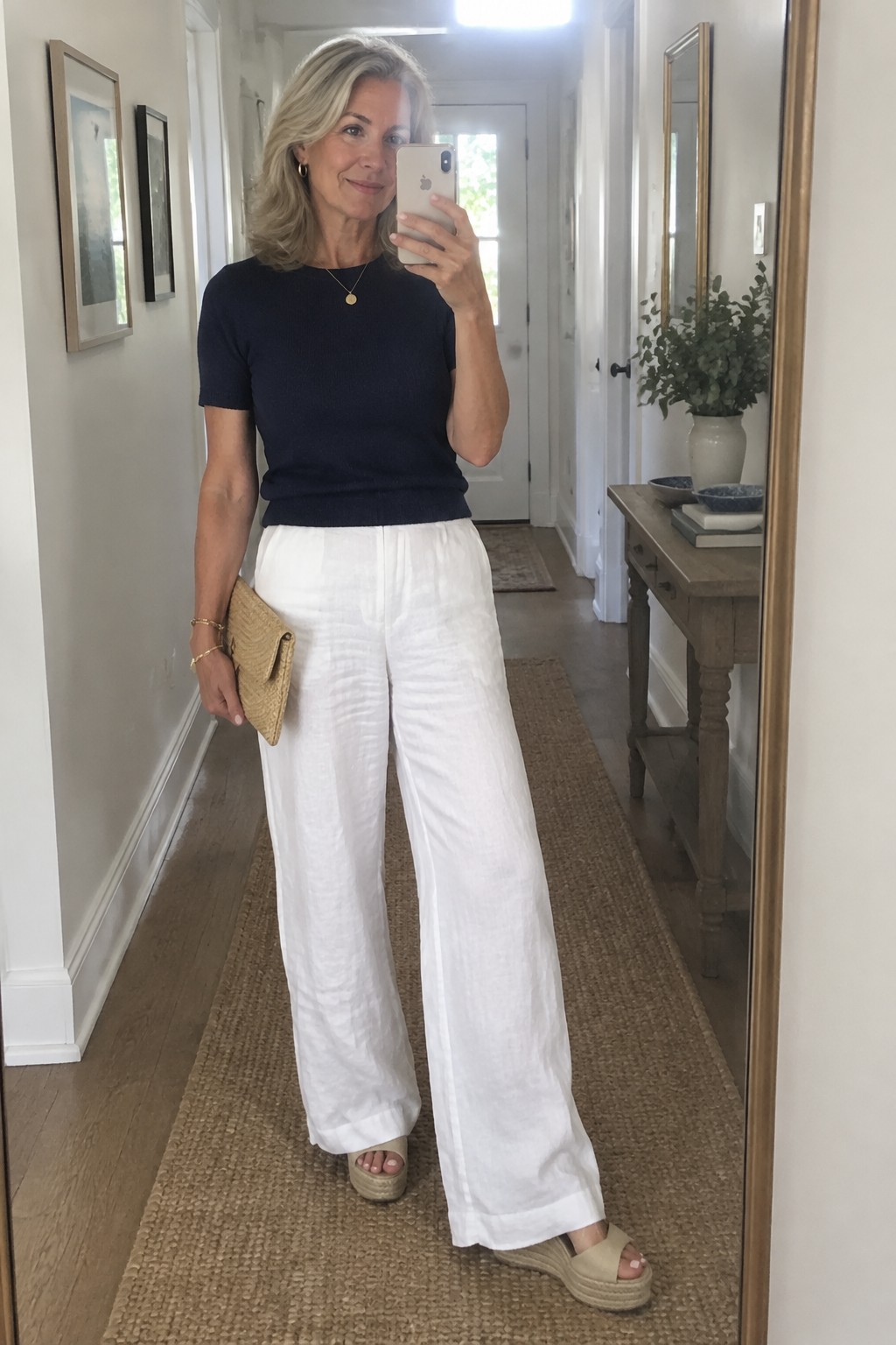 Woman in navy top and white wide-leg pants taking mirror selfie in hallway