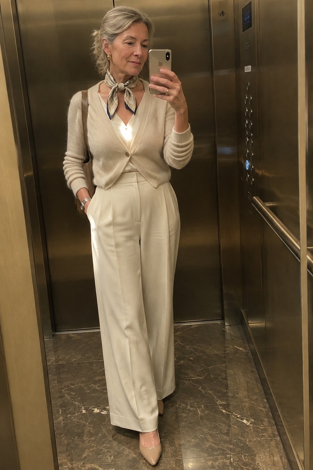Woman in cream cardigan and white wide-leg pants taking selfie in elevator