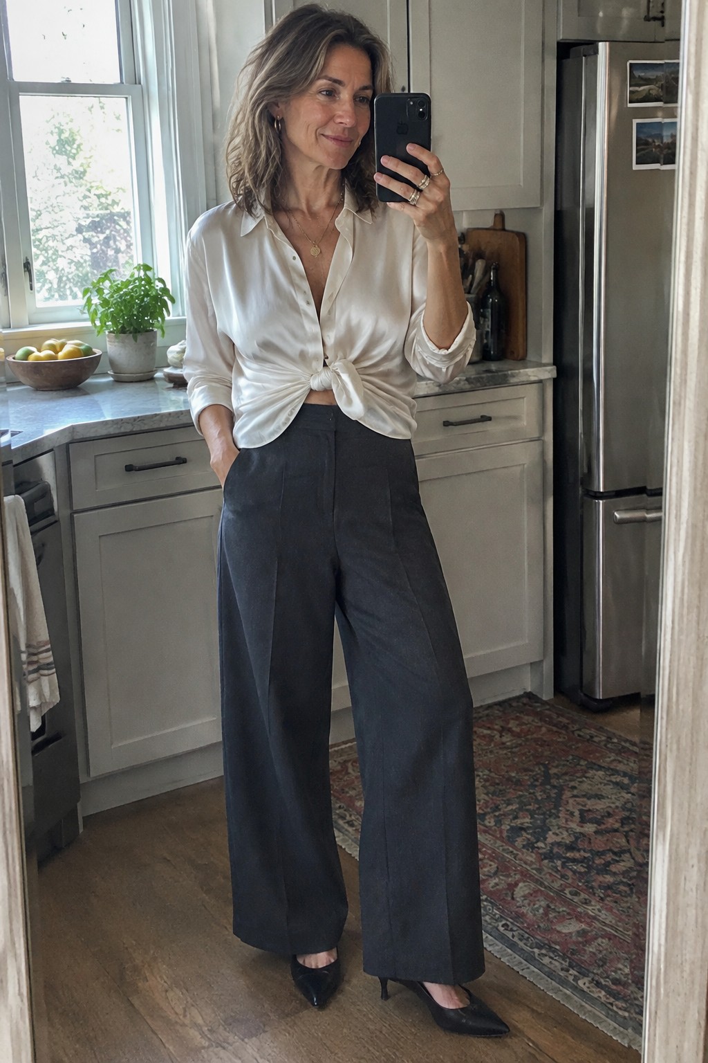 Woman in white knotted blouse and dark wide-leg pants taking kitchen selfie