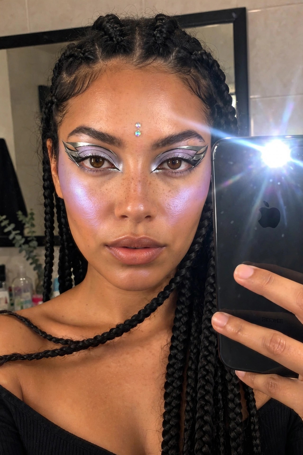 Close-up of metallic silver winged eyeliner with purple eyeshadow and a small forehead gem on a woman with long black braids.