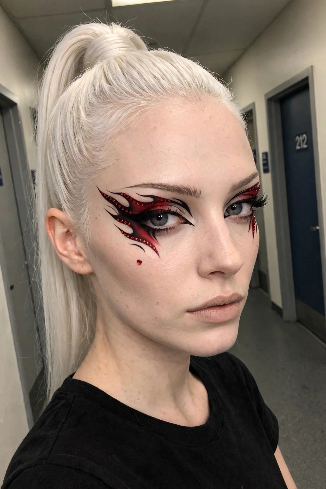 Close up of dramatic red and black flame shaped eye makeup with rhinestones tracing the edges and a small red gem on the cheek.
