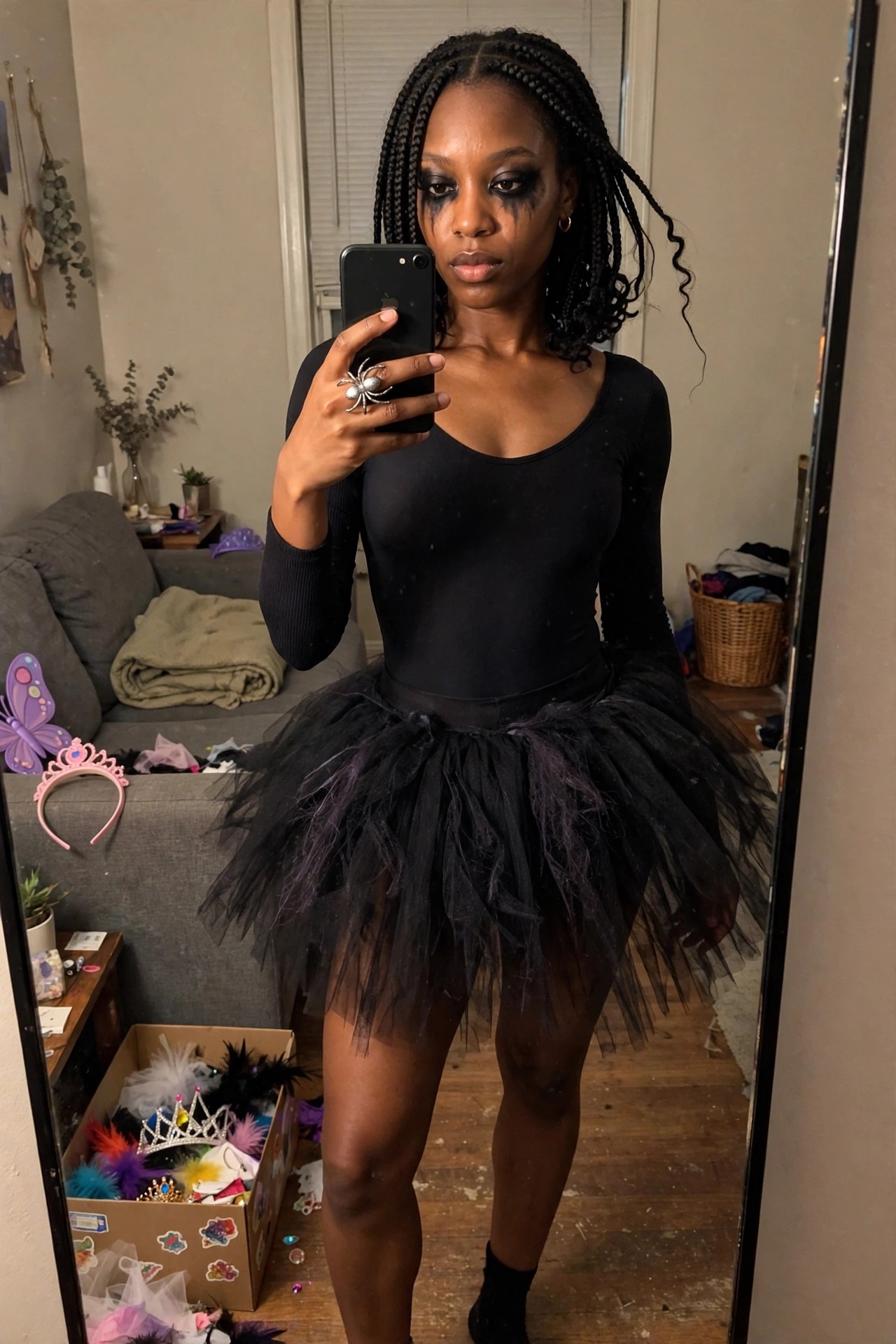 Woman wearing black long sleeve bodysuit and black tutu skirt holding phone with large spider ring while showing dark eye makeup with streaks.
