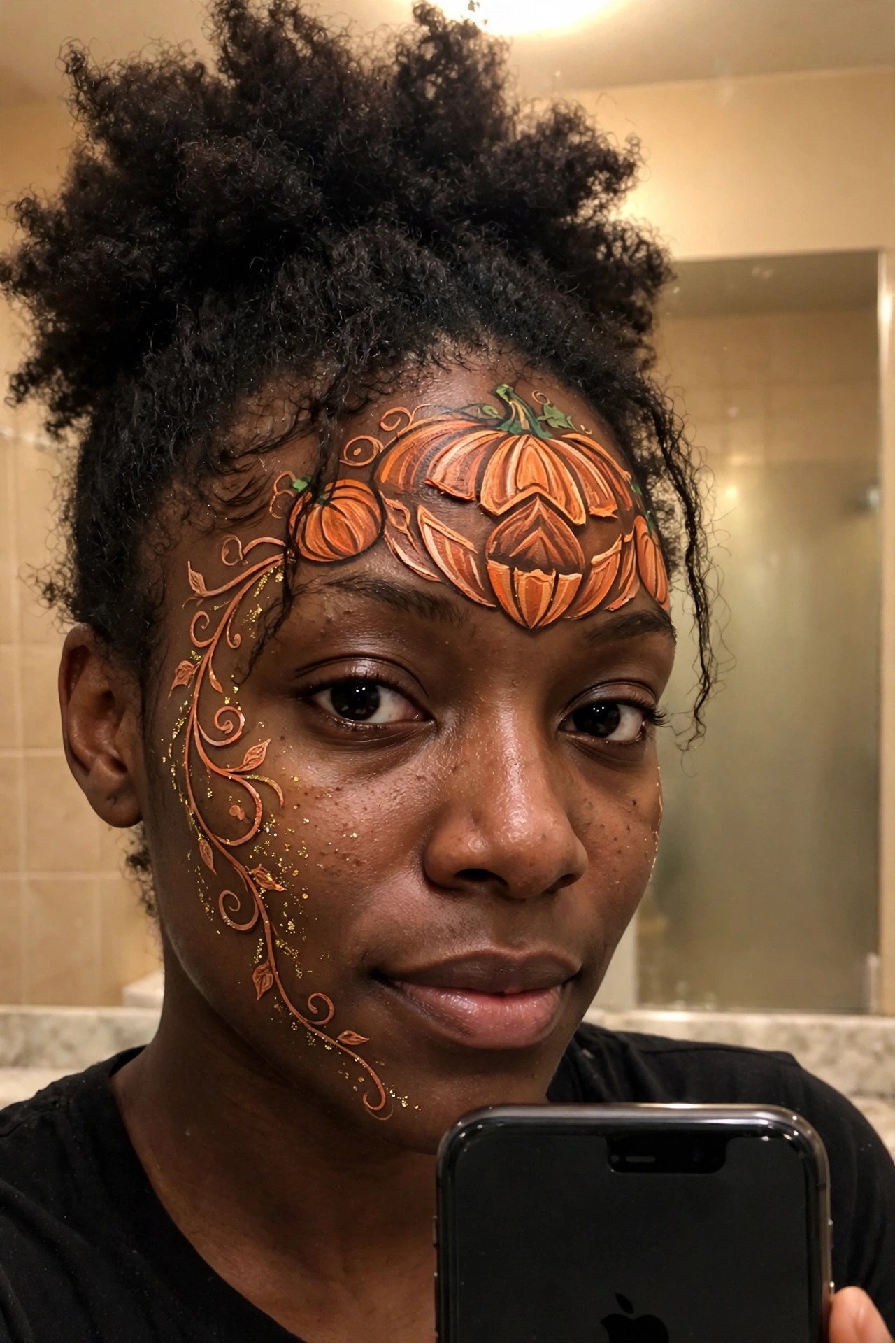 Close up of pumpkin face paint covering the forehead with one large central jack o lantern and smaller pumpkins around it plus swirling vine details extending onto the cheek with gold glitter accents.