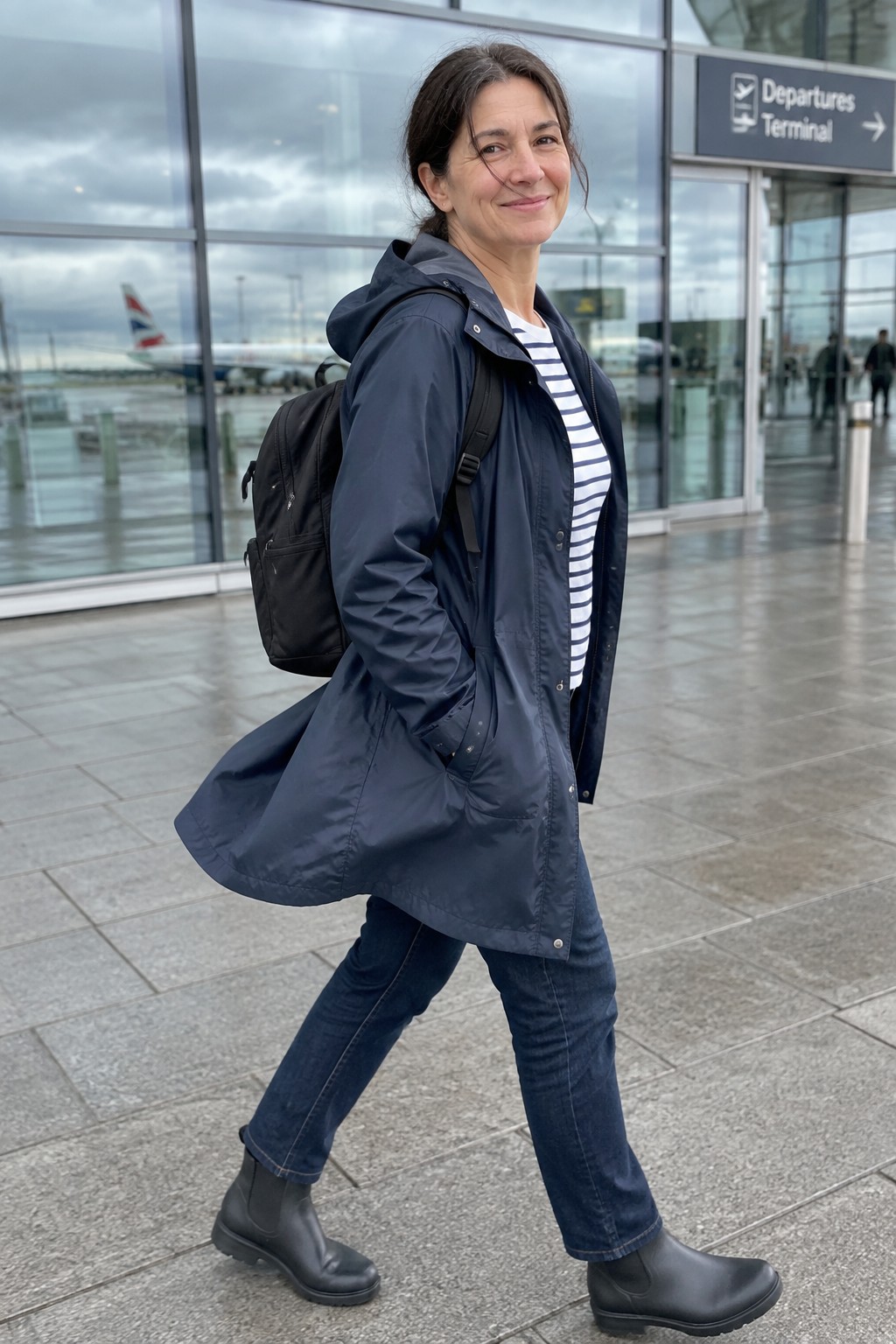 Woman in navy raincoat and black boots walking at airport terminal with backpack