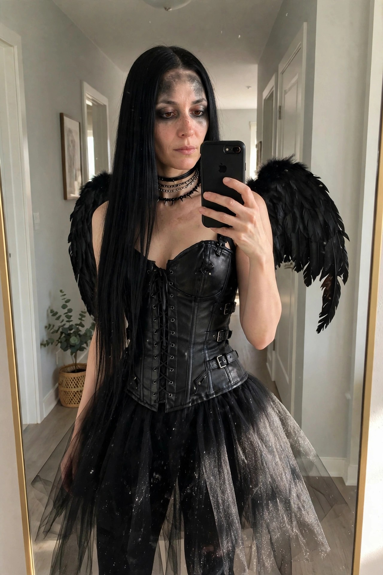 Woman wearing a fallen angel costume with large black feathered wings, black leather corset, black glitter tulle skirt, long straight black hair, and dark eye makeup.