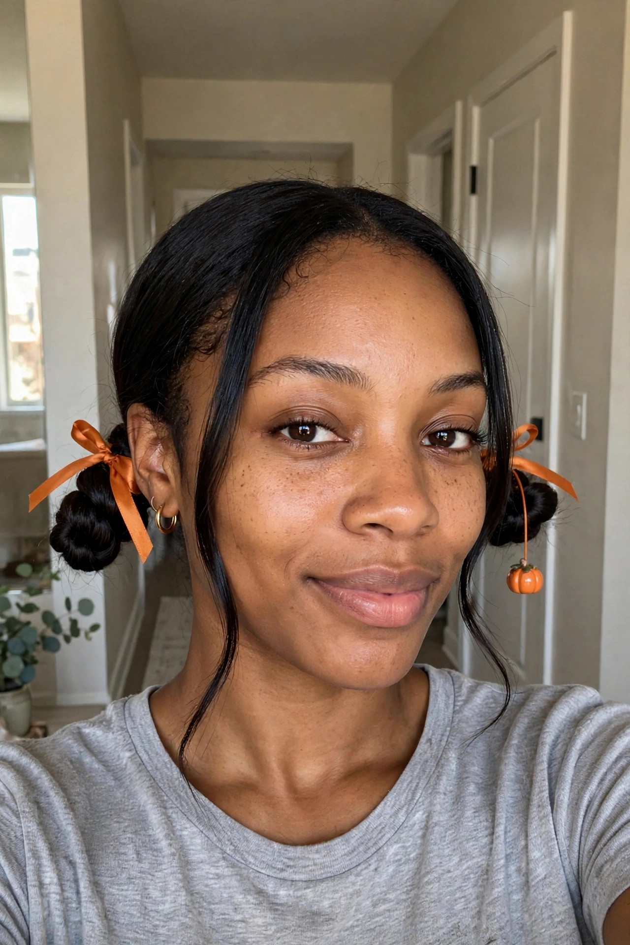 close up of two small space buns tied with orange satin ribbons and a dangling pumpkin charm on one side