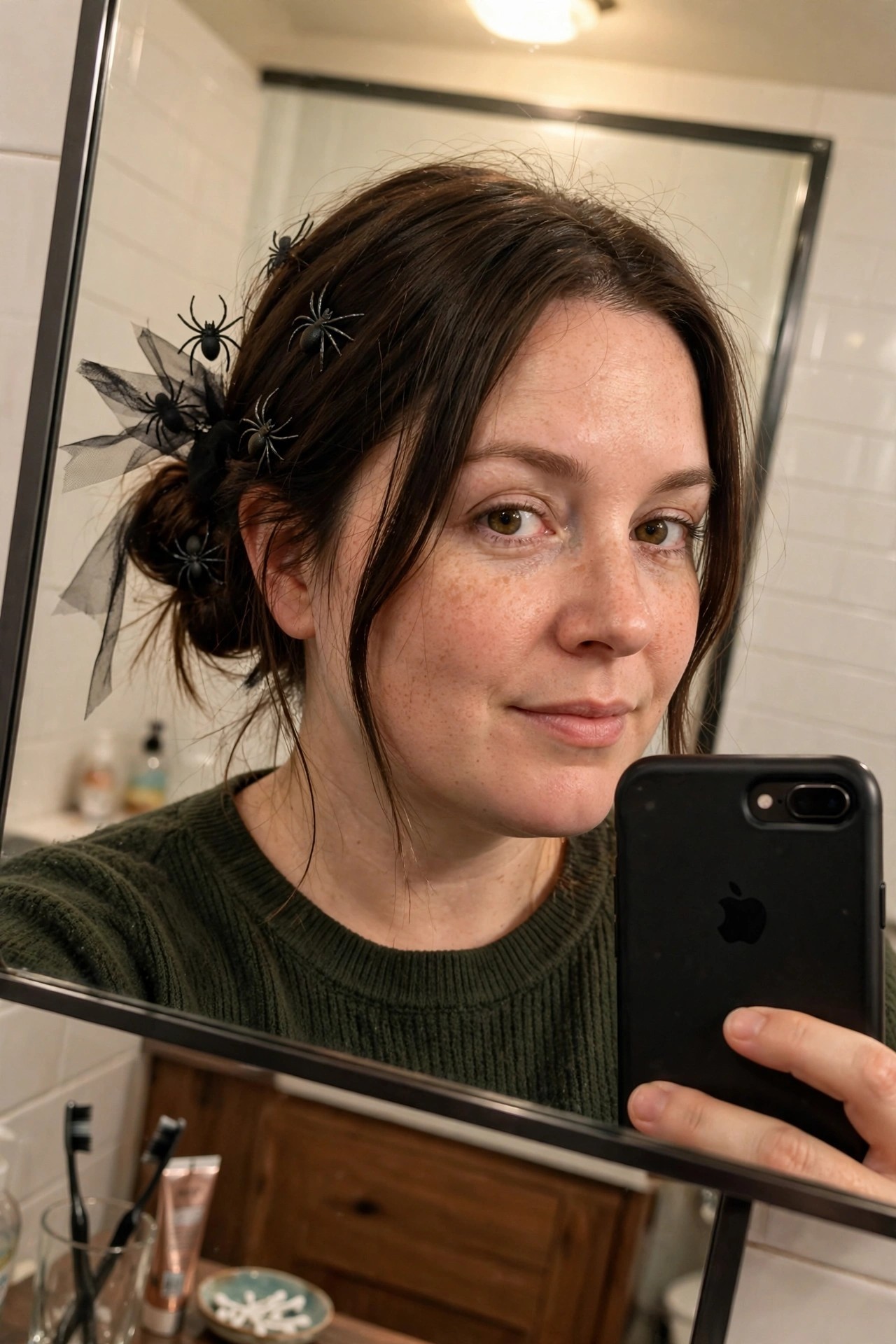 Woman with brown hair in a low messy bun decorated with multiple small black plastic spiders and a black tulle bow accent.