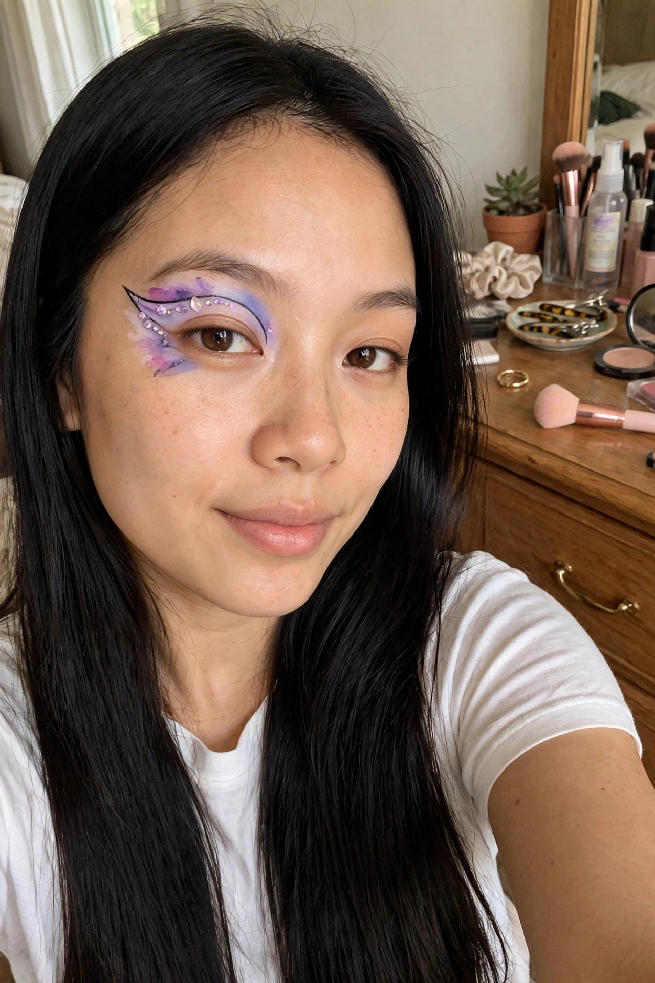 Close up of eye makeup with purple blue and pink watercolor wash a black winged liner and scattered iridescent rhinestones forming a butterfly wing shape.