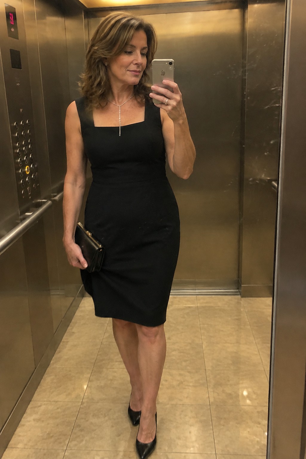 Woman in black dress taking selfie with phone inside elevator