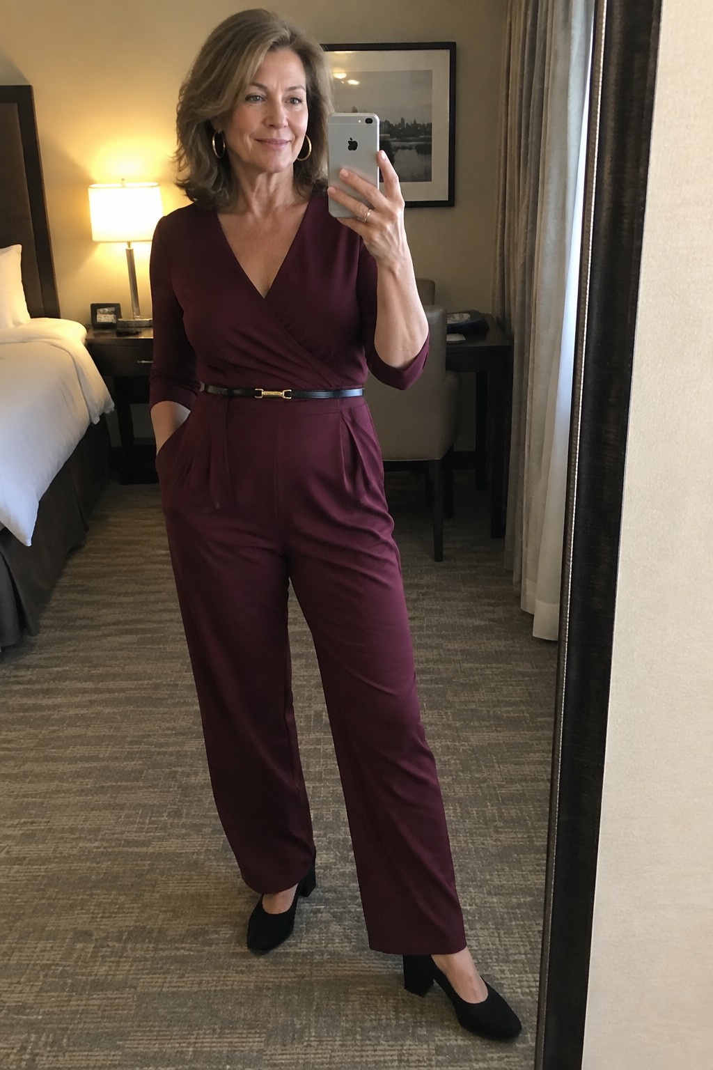 Woman in maroon jumpsuit with black belt taking mirror selfie in hotel room