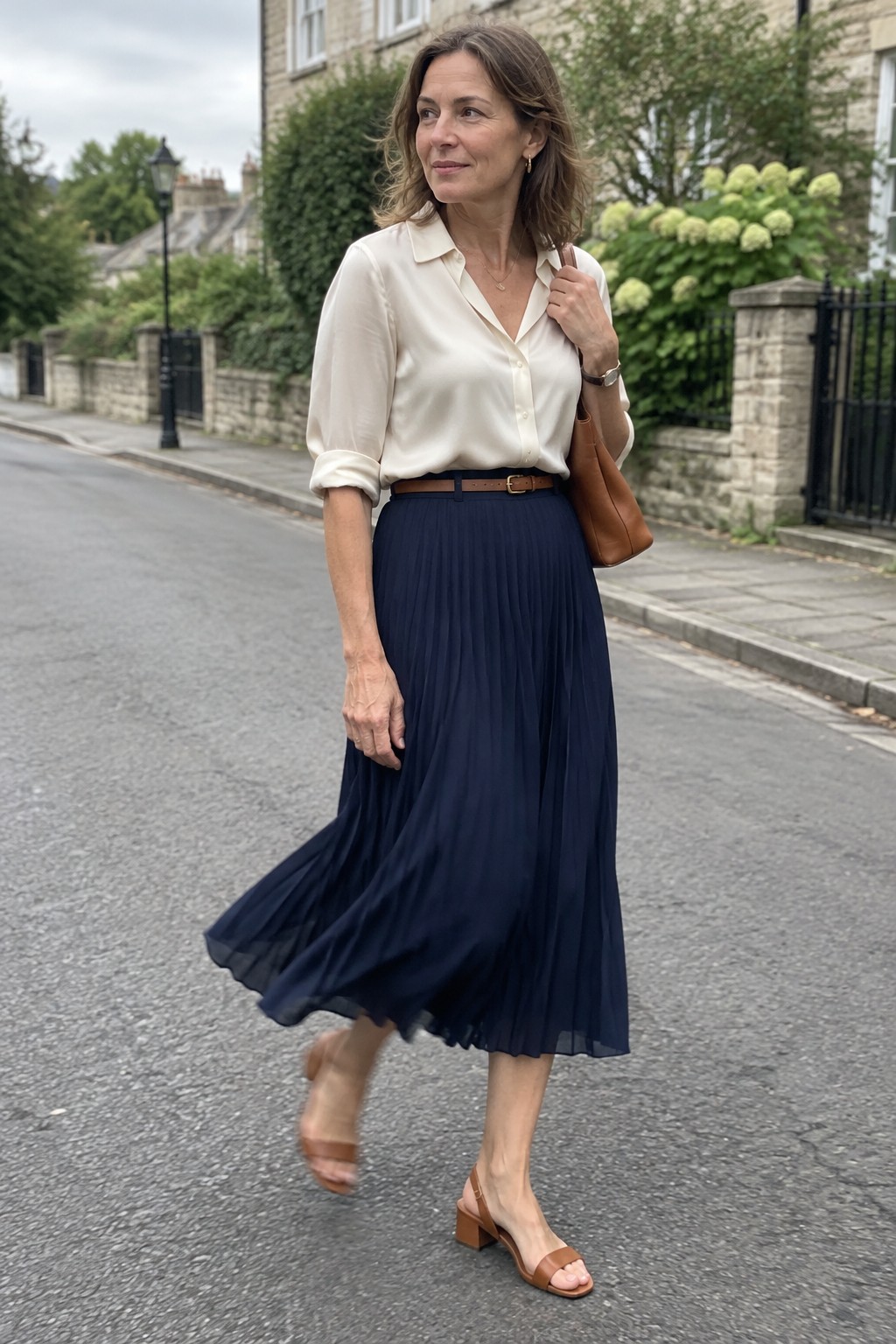 Woman in cream blouse and navy pleated skirt walking on residential street