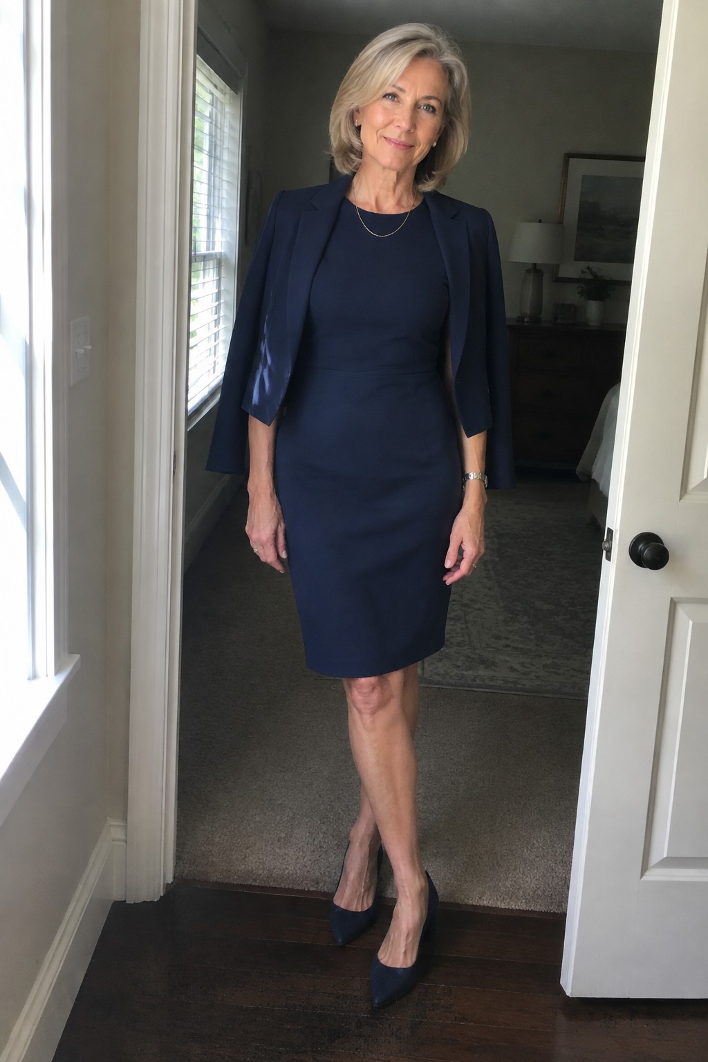 Blonde woman in navy blue dress and cape jacket standing in home hallway